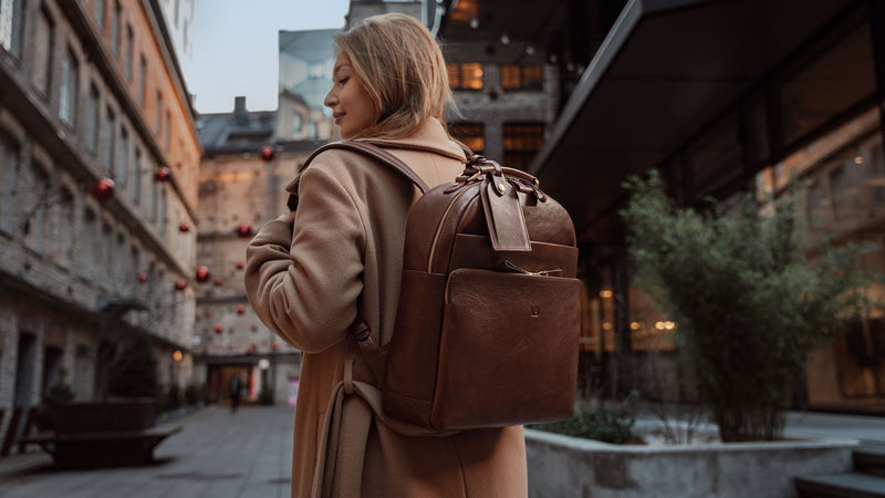 A woman in a beige coat wearing a brown Von Baer Liberty stylish full-grain leather backpack.