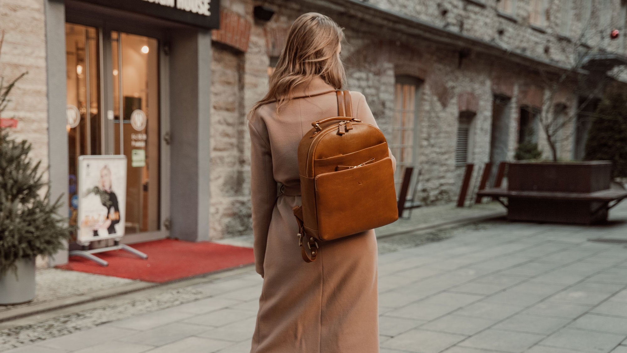 Von Baer Liberty stylish women's full-grain leather backpack in tan, worn by a woman in a beige coat (slider)