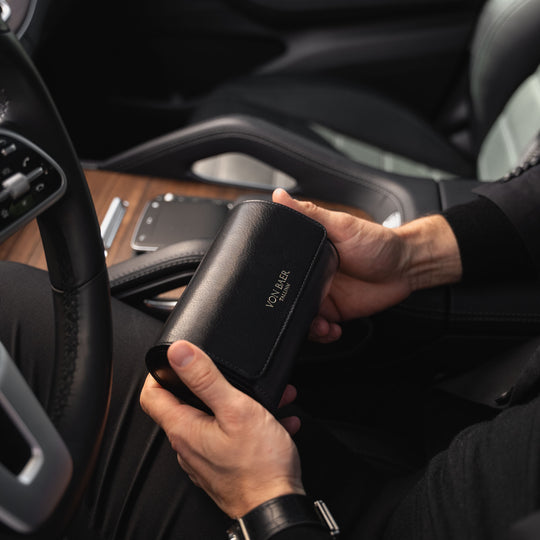 A man in a Mercedes car holding a black Von Baer luxury full-grain leather watch roll case with two slots.