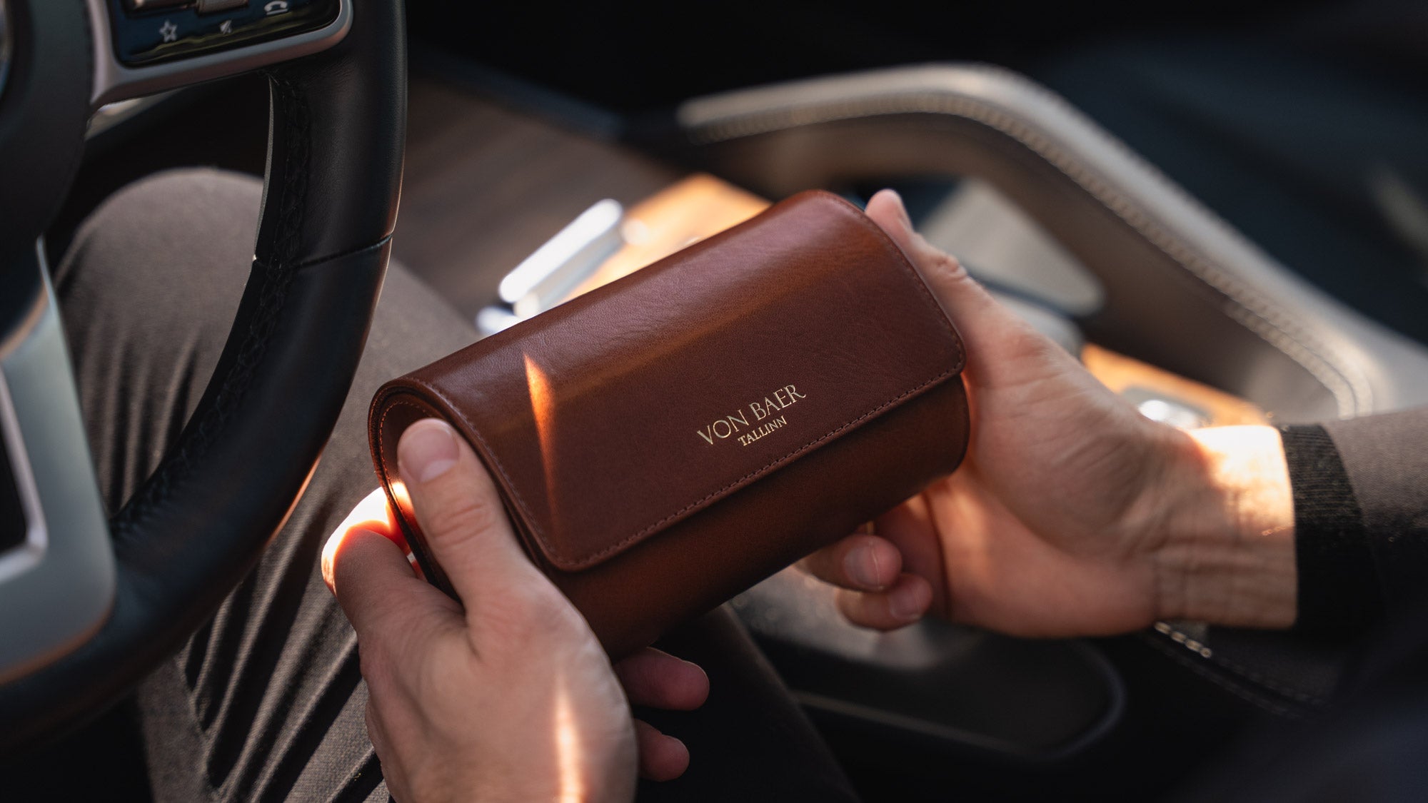 A brown Von Baer luxury full-grain leather watch roll case with two slots, held by a man in a Mercedes car.