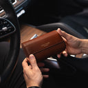 A man in a Mercedes car holding a brown Von Baer luxury full-grain leather watch roll case with two slots.