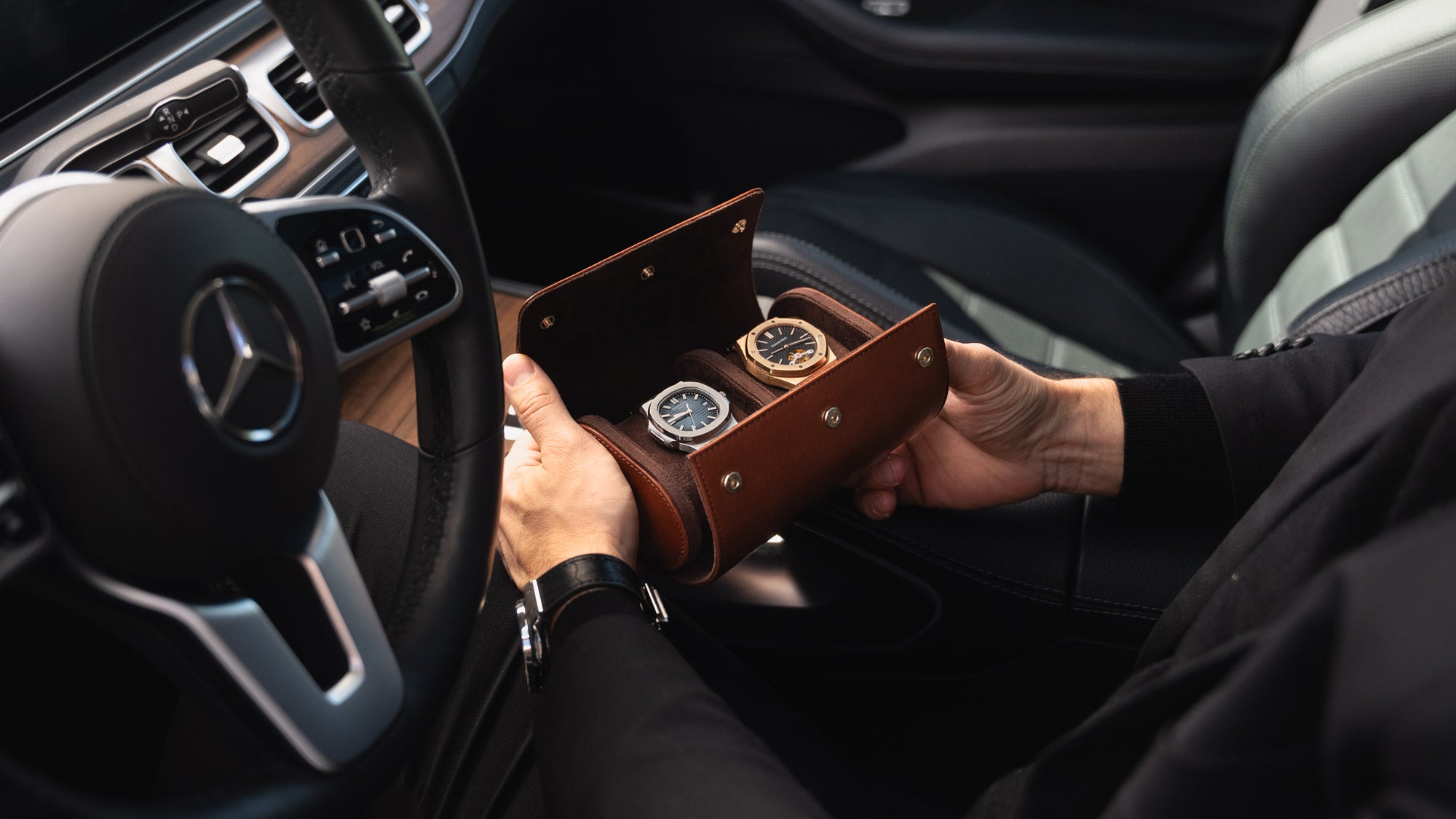 A man in a Mercedes car holding an opened brown Von Baer luxury full-grain leather watch roll case with two slots, showing watches inside.