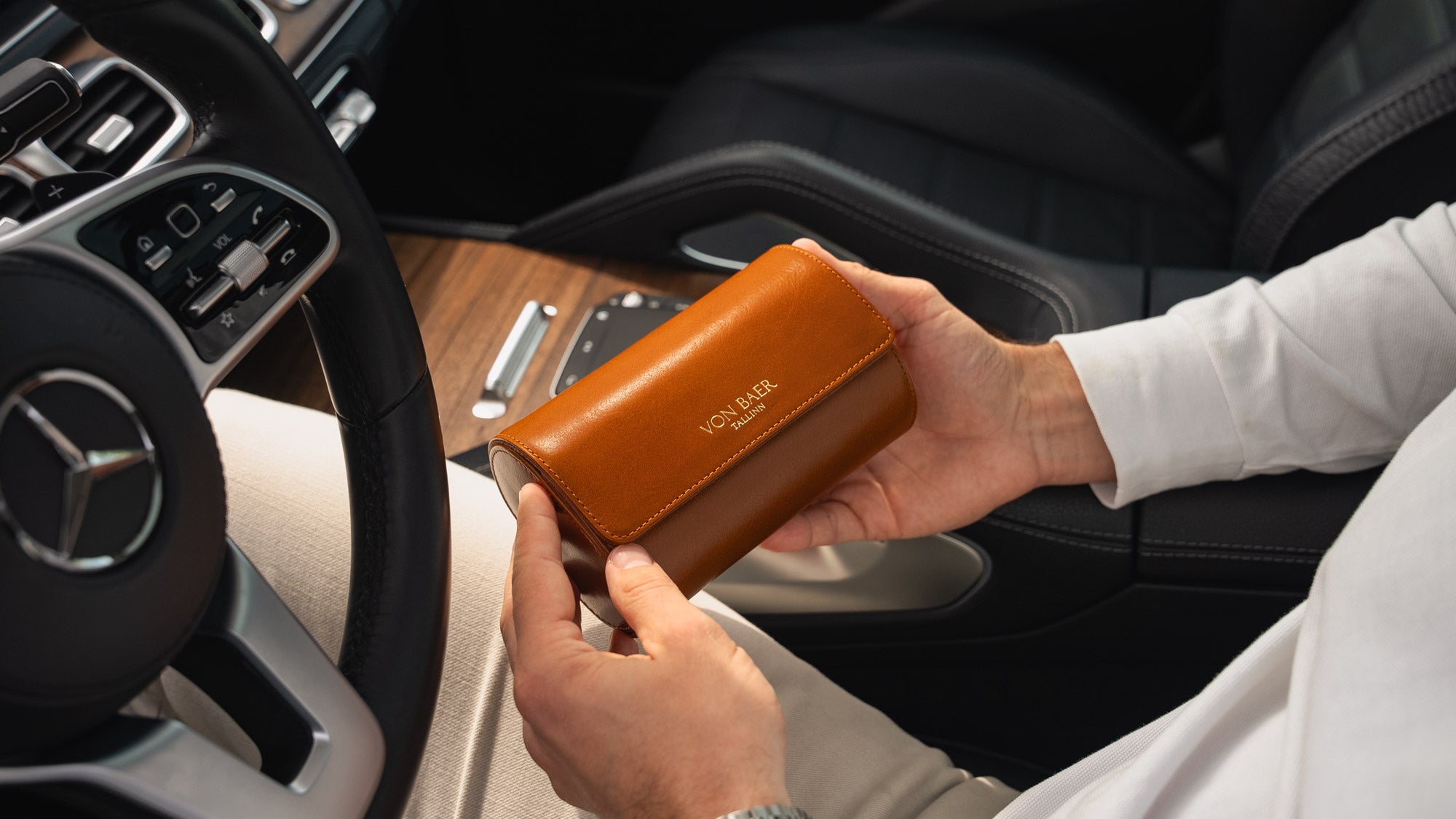A tan Von Baer luxury full-grain leather watch roll case with two slots, held by a man in a Mercedes car.