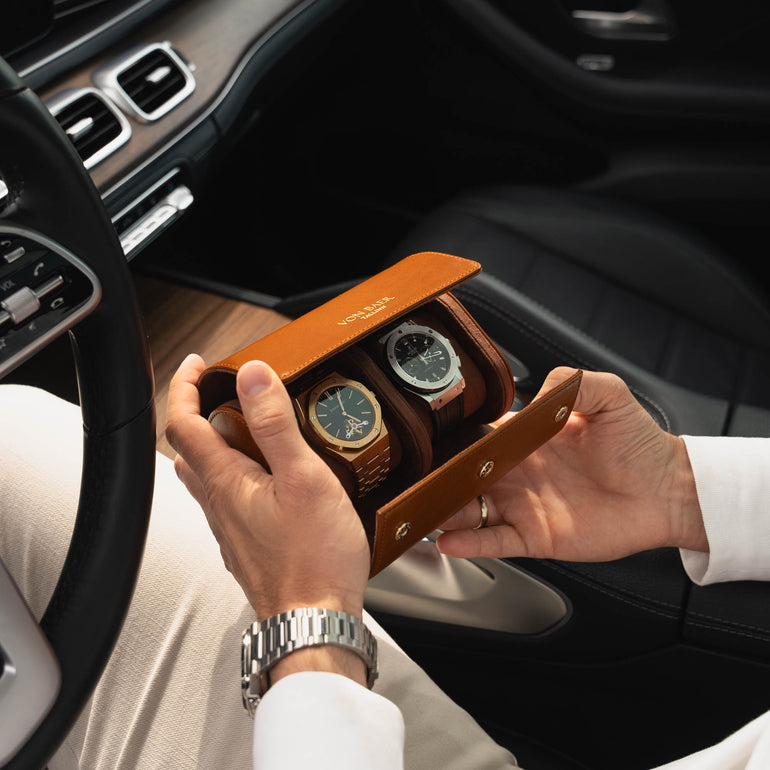 A man in a Mercedes car holding an opened tan Von Baer luxury full-grain leather watch roll case with two slots, showing watches inside.