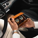 A man in a Mercedes car holding an opened tan Von Baer luxury full-grain leather watch roll case with two slots, showing watches inside.