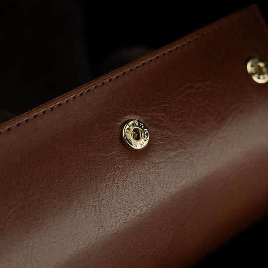 A close-up of the metal button hardware on a brown Von Baer luxury leather watch roll.