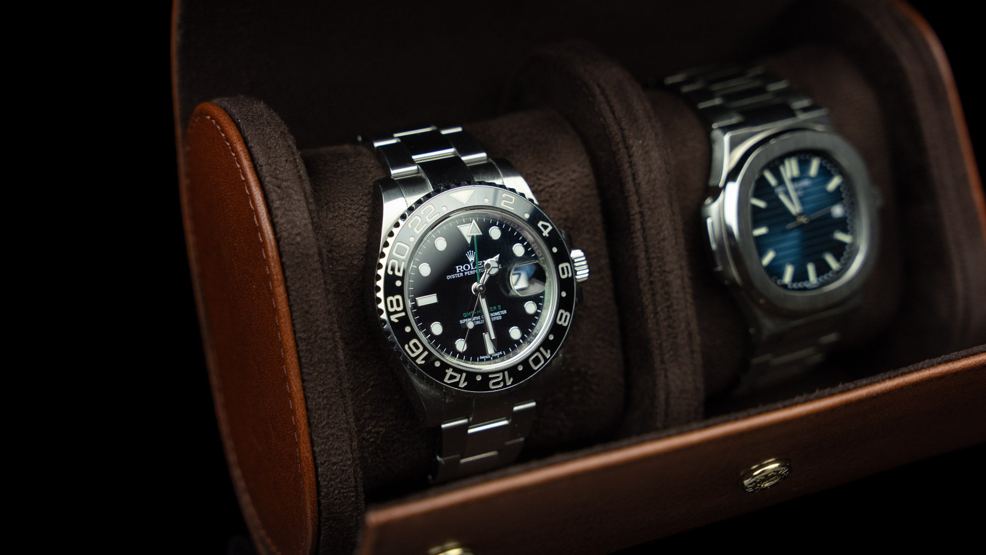 A brown watch roll case by Von Baer holding two watches, a Rolex and a Patek Philippe.