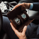 A brown Von Baer luxury leather watch roll with a Rolex watch inside, in the hands of a handsome man in a Porsche car.