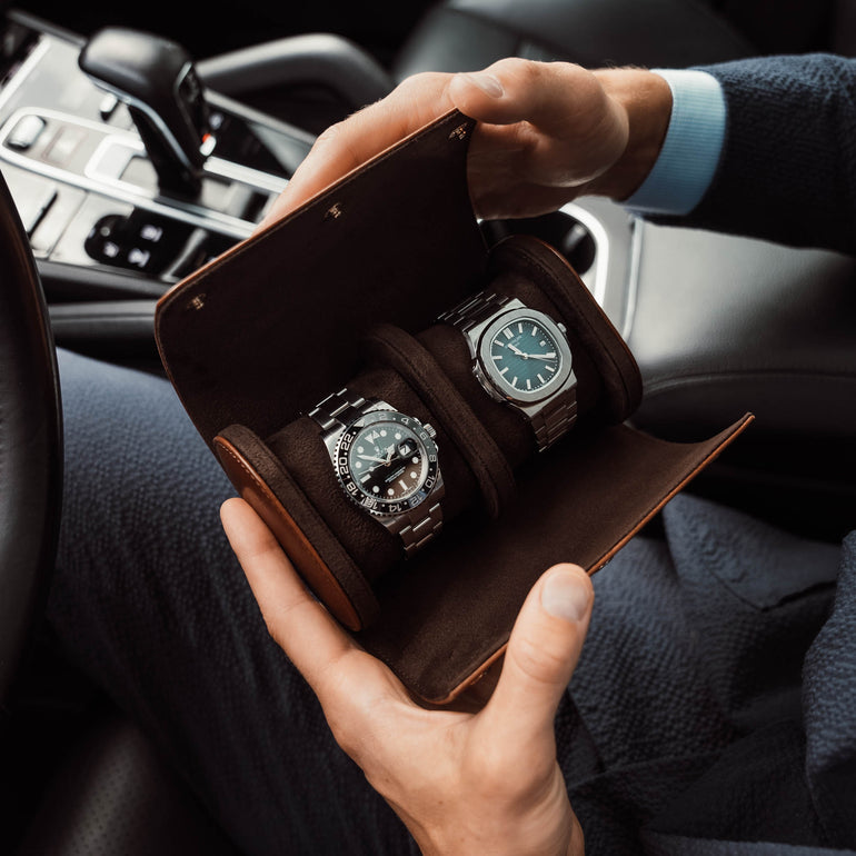A brown Von Baer luxury leather watch roll with a Rolex watch inside, in the hands of a handsome man in a Porsche car.