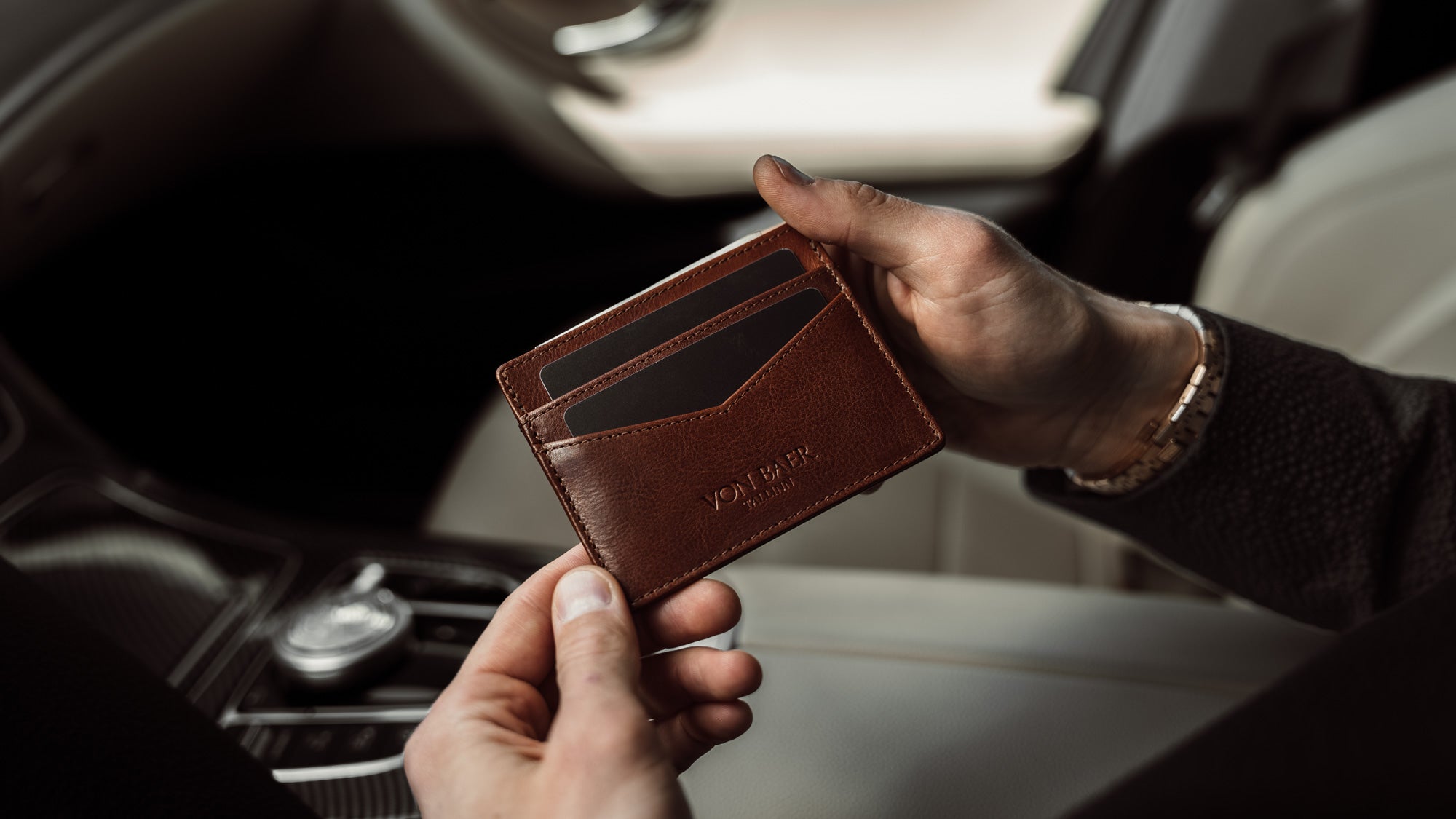 A brown Von Baer minimalist slim leather card holder for men is shown inside a luxurious car.