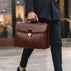 brown leather briefcase carried by the top handle by male model in suit