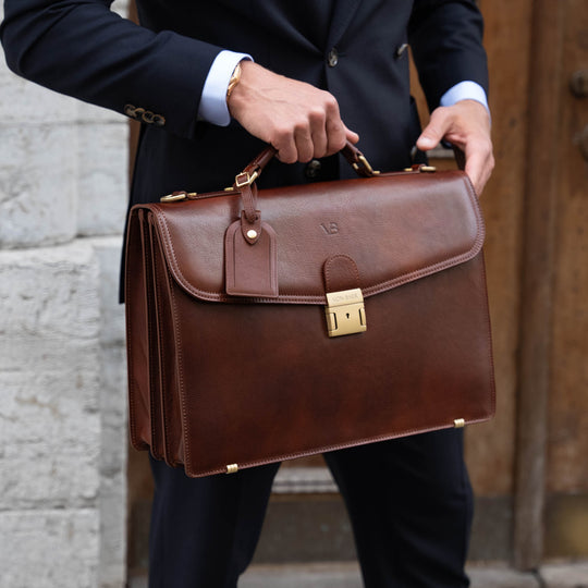 A large, brown Von Baer No.1 full-grain leather briefcase for work and documents with a luggage tag, held by a man in a suit