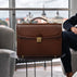 Large luxury men’s leather briefcase for work, documents, and laptop on a city office background.
