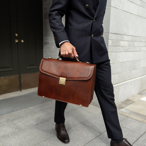 A large, brown Von Baer No.1 luxury men's leather briefcase for work and documents, held by a businessman in a suit