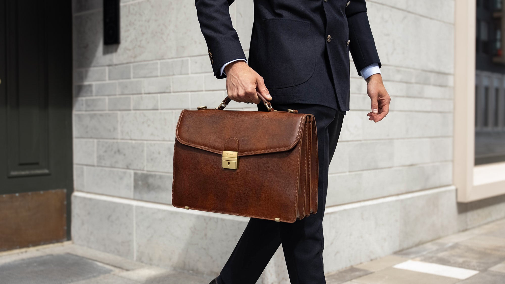 A large, brown Von Baer No.1 luxury men's leather briefcase for work and documents, held by a man in a suit