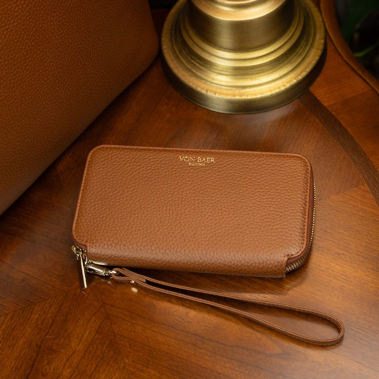 Von Baer origin leather purse on a vintage table near an old lamp and a luxury tote bag