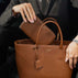 Von Baer Origin Portmonnaie cognac tan full-grain pebbled leather wallet being placed inside an Estelle small tote bag by a person in a dark blazer.