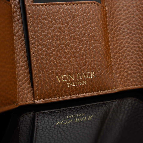 Von Baer Reverie compact cognac pebbled leather wallet for women, shown in close-up highlighting the gold foil Von Baer Tallinn logo embossed on a leather tab and the mirrored branding on the black leather interior section