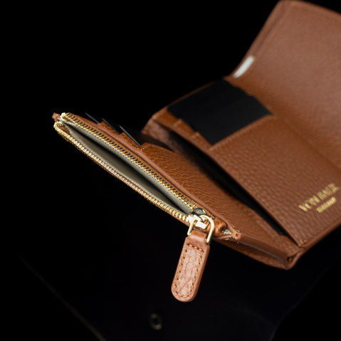 Von Baer Reverie elegant cognac pebbled compact leather women's wallet, shown open in close-up to highlight card slots, a black interior card holder, and a gold-tone zippered coin pocket with a leather pull tab against a black background