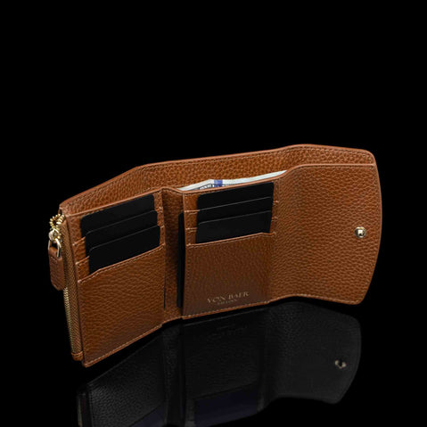 Von Baer Reverie luxury compact cognac pebbled leather wallet for women, shown open with multiple card slots, a gold-tone zipper, and a small gold logo on the interior, displayed on a reflective black surface