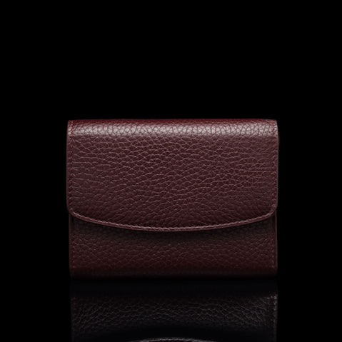 Von Baer Reverie compact burgundy pebbled leather wallet for women with a fold-over flap, shown centered in a front view against a solid black background with a subtle reflection.