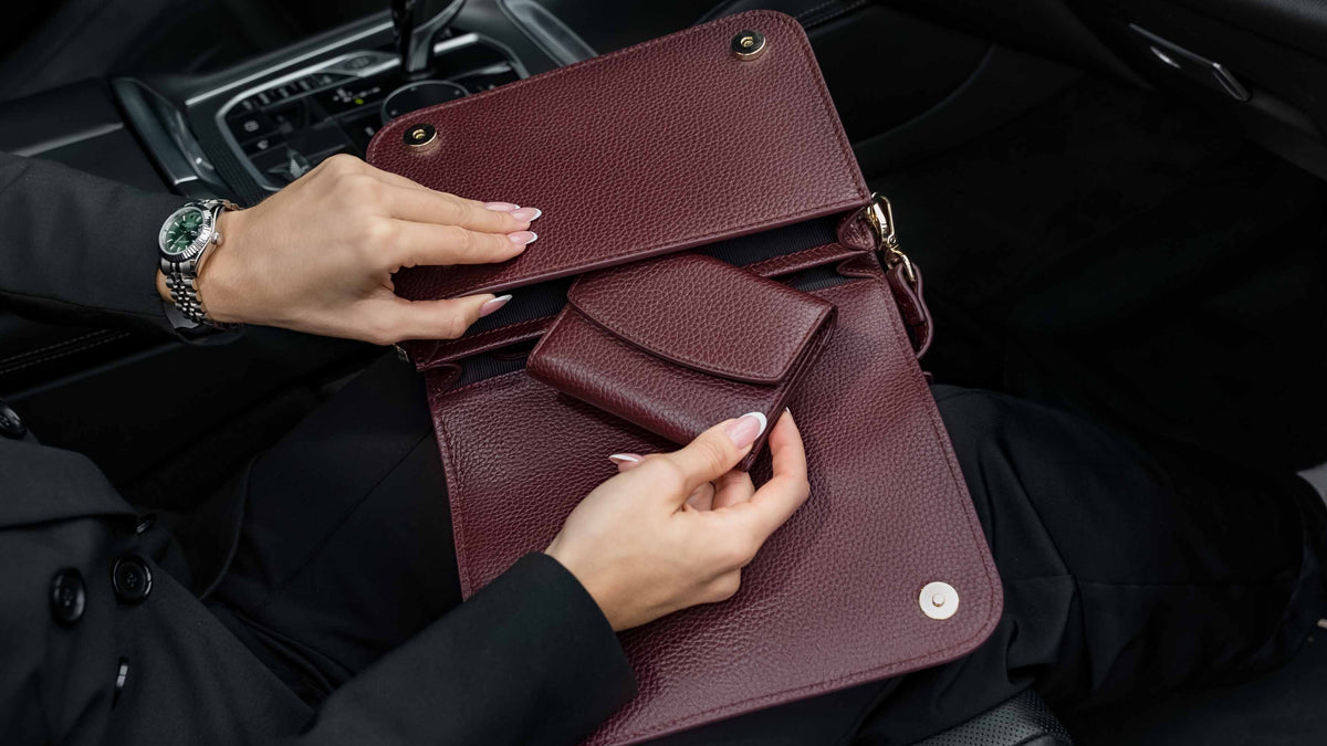 Von Baer Reverie burgundy small full-grain leather wallet for women shown open inside an Isabella Grande large leather crossbody bag, held by a person in a black blazer inside a car interior to display storage details.
