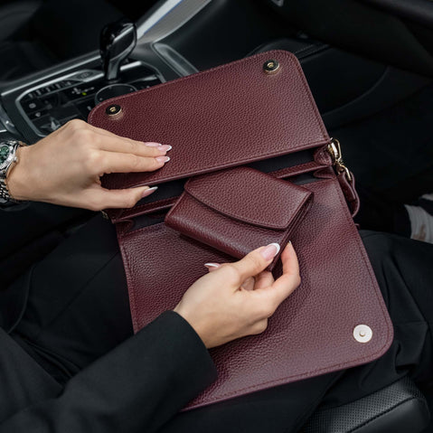 Von Baer Reverie small full-grain leather wallet and Isabella Grande large burgundy leather crossbody bag, shown open by hand inside a car to highlight the matching pebbled leather texture and interior compartments