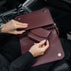 Von Baer Reverie small full-grain leather wallet and Isabella Grande large burgundy leather crossbody bag, shown open by hand inside a car to highlight the matching pebbled leather texture and interior compartments