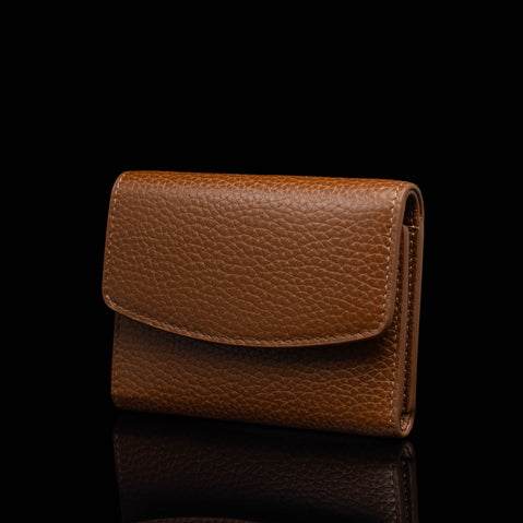 Von Baer Reverie small luxury cognac pebbled leather wallet for women, shown closed in a three-quarter view highlighting its elegant front flap and compact design against a reflective black background