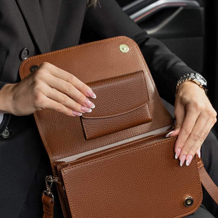 Von Baer Reverie women's full-grain compact leather wallet and Isabella Grande large cognac leather crossbody bag, shown open in a close-up to highlight the pebbled leather texture and spacious interior compartments, held by a woman wearing a black blazer