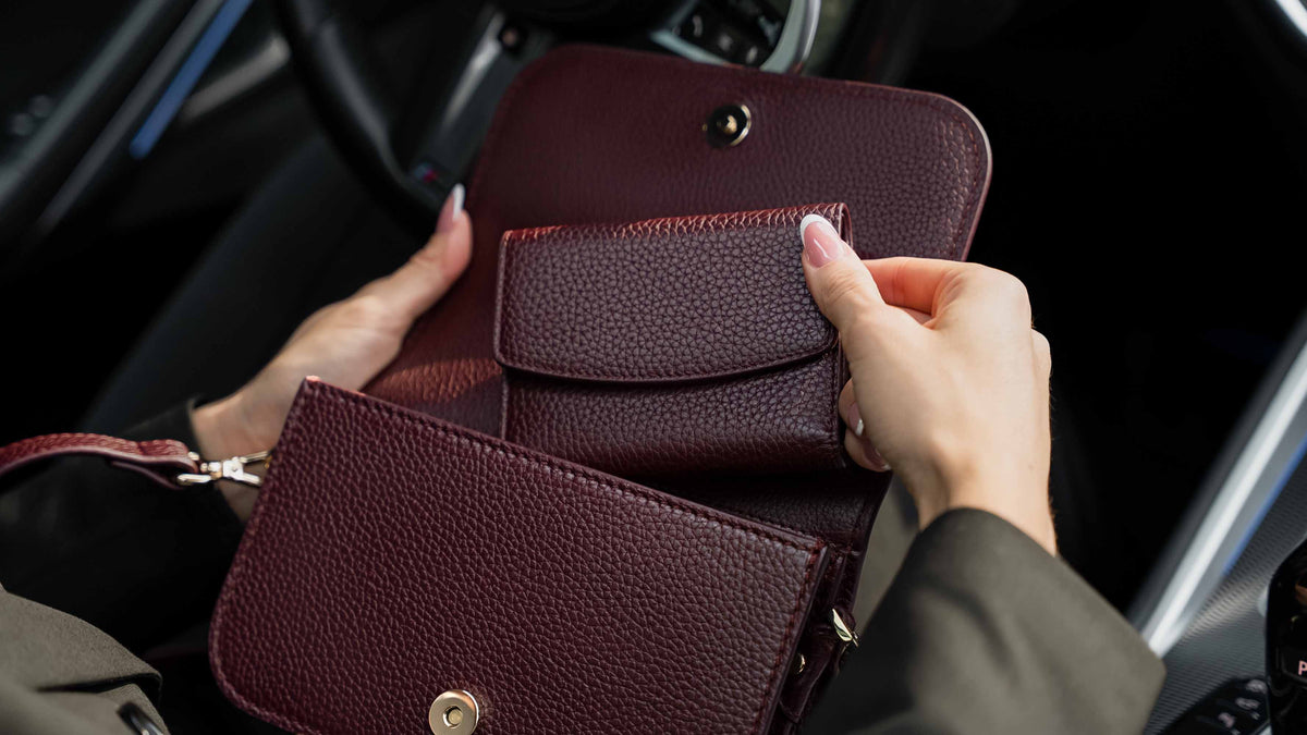 Von Baer Reverie burgundy women's leather wallet shown open inside an Isabella small leather crossbody bag for women, held by a person in a car interior displaying storage details.