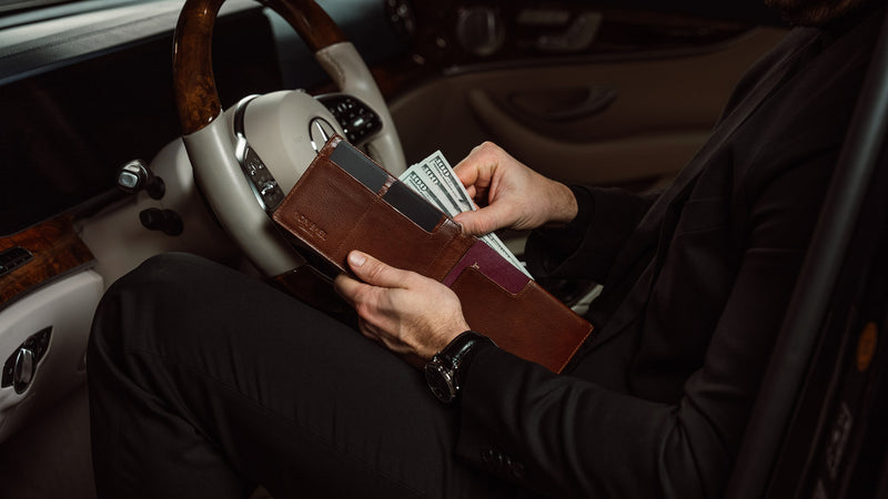 A lifestyle shot of the Von Baer slim leather passport holder and RFID wallet in brown, carried by a man while counting cash, showcasing its practicality and stylish design for travel.