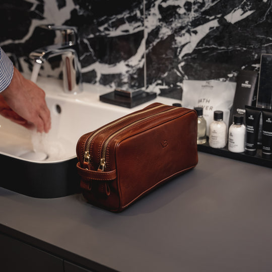 Von Baer superior high-quality luxury full-grain leather wash bag in brown, placed in the bathroom while a man washes his hands.