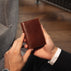Von Baer Tallinn element leather card case in brown held by a male model in a luxury hotel setting