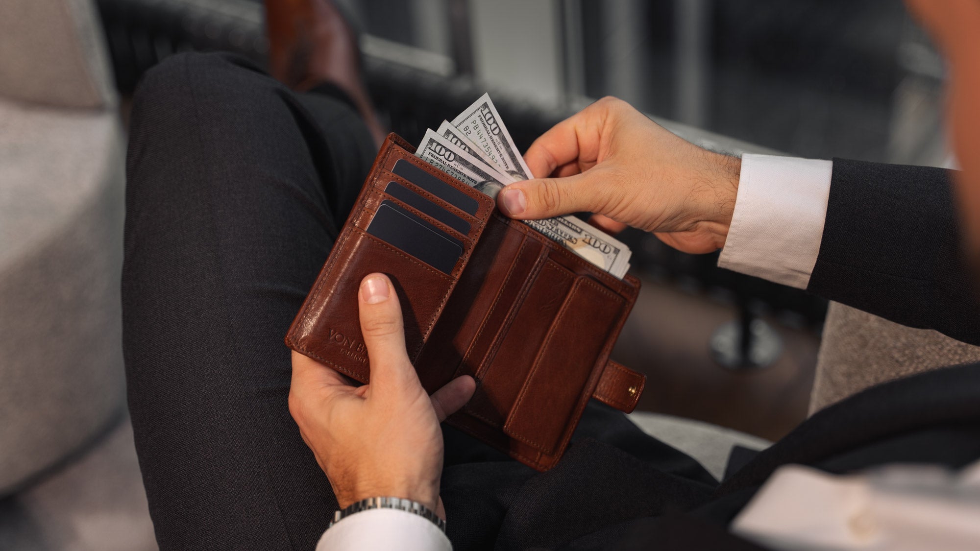 Von Baer Tallinn Heritage large men's high-quality leather trifold wallet held by a male model in luxury apartments with dollars, highlighting elegance and functionality.