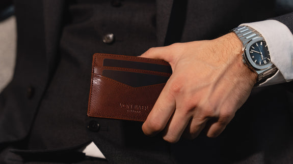 Von Baer Tallinn minimalist high-quality luxury leather card holder in brown, held by a well-dressed man in a black suit, slider