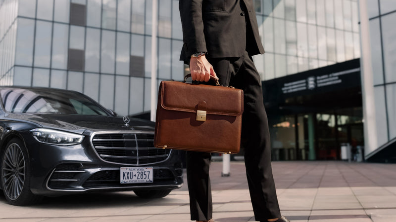 Von Baer No.3 men's traditional brown leather briefcase, held by a man in a suit in front of a modern office building with a Mercedes S-Class parked nearby