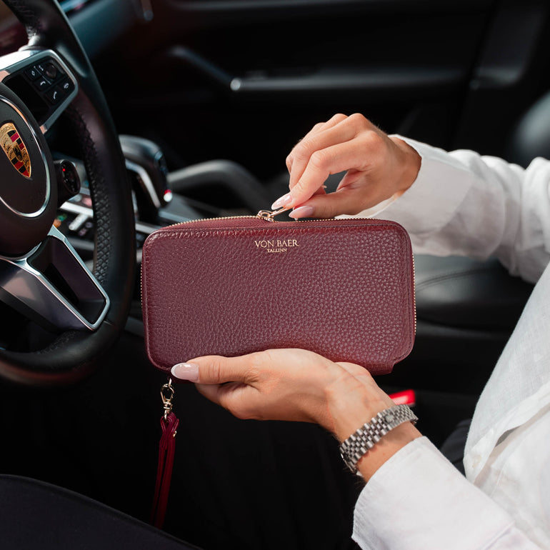 A person holding a premium looking burgundy pebbled leather zip-around wallet with a gold-tone Von Baer logo, set against the background of a car interior.
