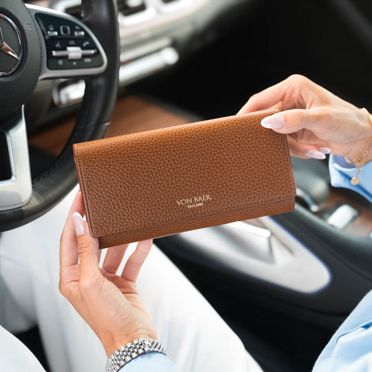 A person holding a tan pebbled leather purse with 'VON BAEr' printed on the front, set against a blurred car interior background.