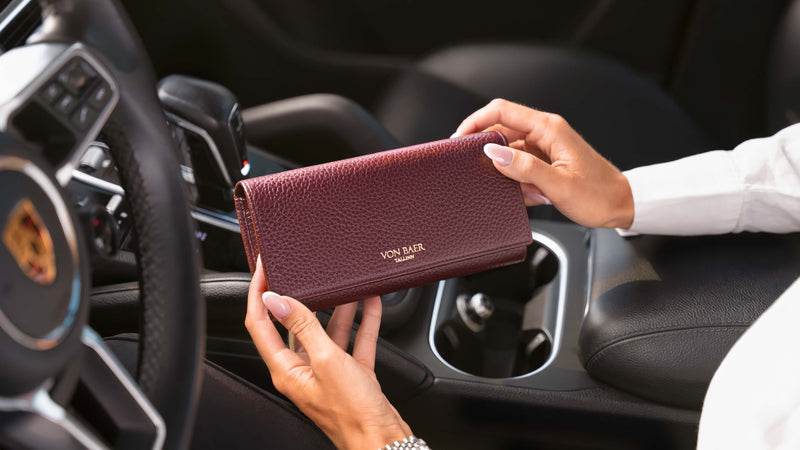 A person holding a premium looking burgundy pebbled leather Von Baer wallet inside a black car interior.