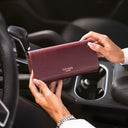 A luxurious burgundy pebbled leather wallet held by a person inside a car, with the gold 'VON BAER' logo visible on the front.