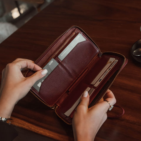 Von Baer W2 Lard full-grain leather purse in red held by a woman in a coffee shop, with her hand taking out a bank card.