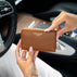 A person holding a classic tan pebbled leather zip-around wallet with gold lettering that reads 'VON BAER' inside a car interior.