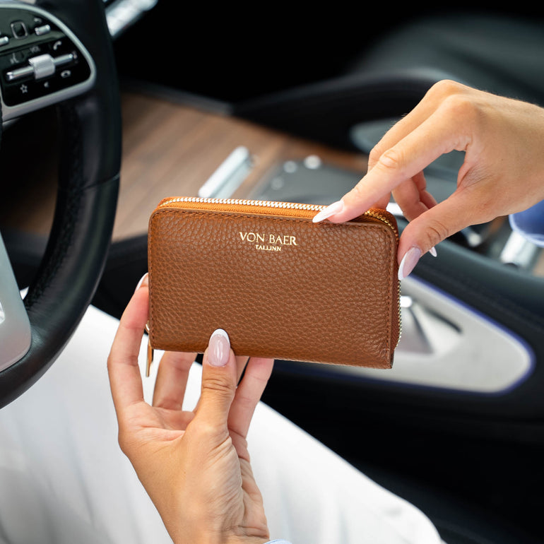 A person holding a classic tan pebbled leather zip-around wallet with gold lettering that reads 'VON BAER' inside a car interior.