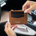 A brown pebbled leather card holder wallet with gold-toned hardware, held by two hands in front of a blurred car interior. The wallet features the brand name 'VON BAER' and 'TALLINN' printed in gold on the front pocket.