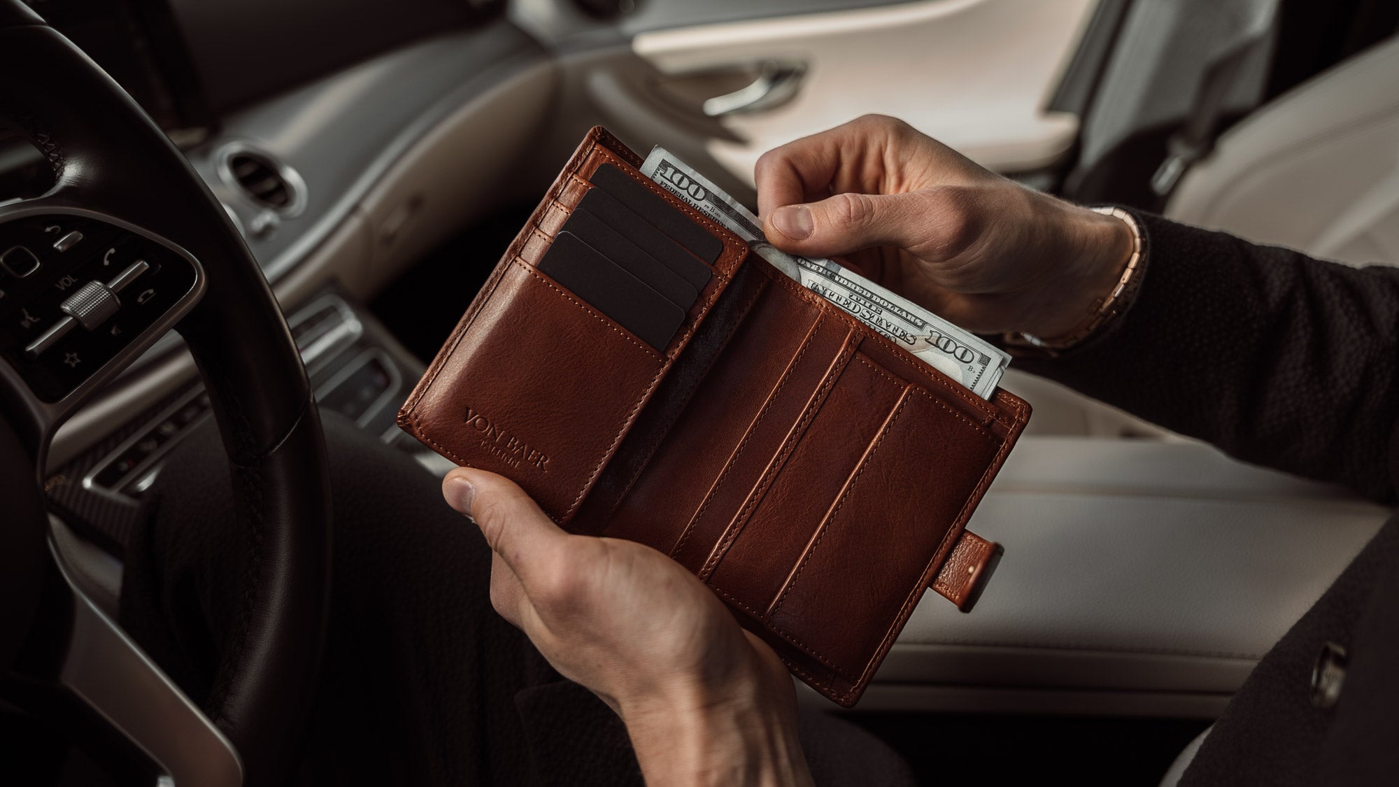 Von Baer Washington premium men's leather trifold wallet in solid brown, with cash in the car, slider.