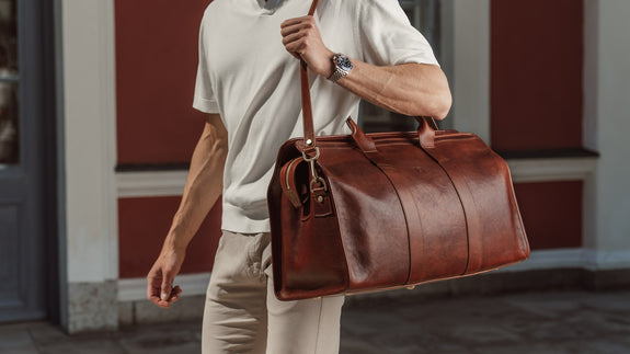 Von Baer Weekender luxury and durable men's leather bag in brown with shoulder strap, carried by a businessman, slider.